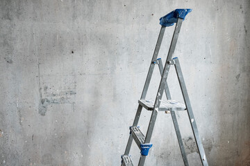 The aluminum ladder against the background of a gray wall. Concept: renovation, finishing, reconstruction of premises.
