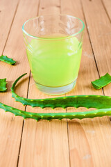 Aloe Vera juice in a glass and fresh aloe leaves on a wooden background. Vertical image.
