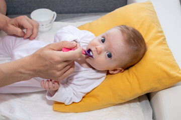 Little baby girl eating rice soup with spoon. Happy little cute daughter with blue eyes. The baby girl is four months old.