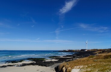 Beautiful view Woljeong Beach with leading line to white windmill at far right at Jeju Island South Korea backed by awesome blue sky background.