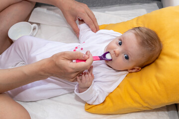 Mother feeding her baby girl with a spoon. Mother giving food to her four-month old baby.