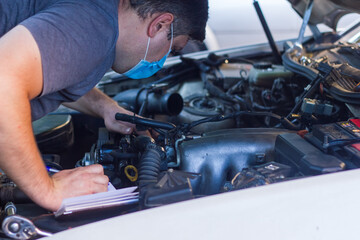 car mechanic on protective mask fixing car engine, auto mechanic is repairing car engine