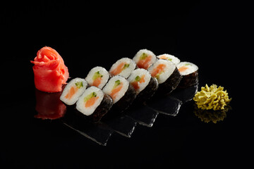 Japanese Cuisine - Appetizing Salmon Sushi Set. Philadelphia Sushi Roll - Maki Sushi with Philadelphia Cheese inside on mirror black background. Smoked salmon rolls served on a plate