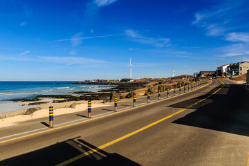 Beautiful view Woljeong Beach besides trunk road providing leading line at Jeju Island South Korea with white windmill at far left backed by awesome blue sky background