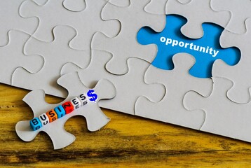 conceptual business opportunity.  Text "opportunity" on missing jigsaw piece on blue surface. Generic beads "business" text on loose piece on rough wooden surface. Selective focus.