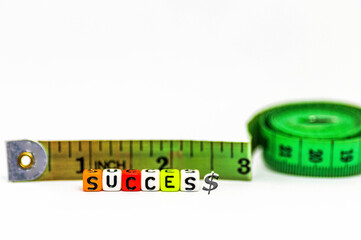 Image of measuring  success concept in life and business. Colorful alphabet beads spelling "succes$" and green measuring tape. Only beads in focus; other in blurs. Gradient bur white background.
