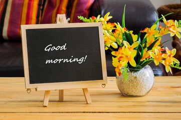 Image of motivational greeting Good morning on chalk board. Besides a decorative green plant in vase. Selective focus on notice board. Others in gradient blur.