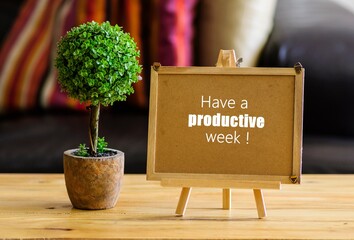 Image of motivational greeting have a productive week on brown mini notice board. Besides a decorative green plant in vase. Selective focus on notice board. Others in gradient blur.