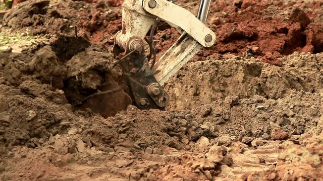 Excavator bucket digs brown clay and sandy soil. Close-up.