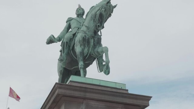 Handheld track shot of Karl Johan statue in front of Royal Palace with red flag in background, in Oslo Norway