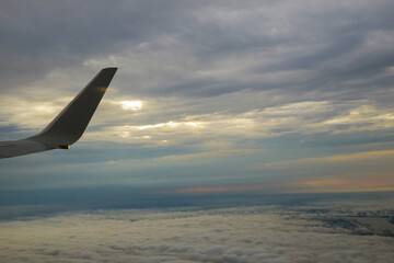 Fototapeta premium Wing of in airplane flying above the morning clouds in altitude during flight.