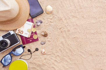 Fototapeta na wymiar Some beach items, a passport and some cash, a smartphone, hat, camera and sunglasses on the sand. Space for text. Holiday, summer and beach concept.
