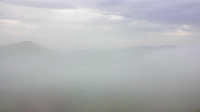Time lapse from the top of the mountain with view on the fogy and cloudy valley. Mountains surrounded with fog. Captured at dawn.