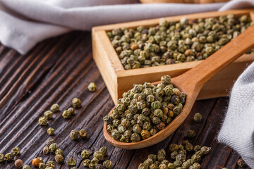 green peppercorns in wooden scoop on rustic background