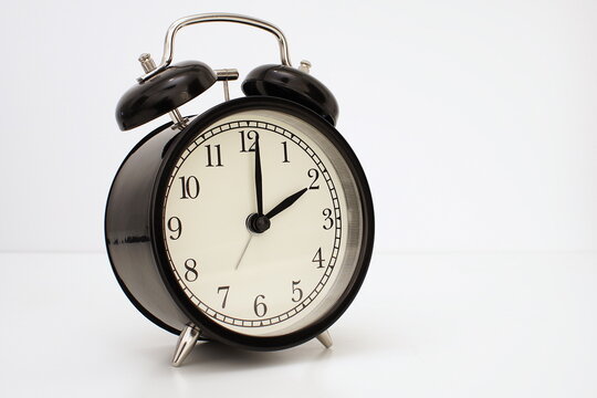 Black vintage alarm clock on table. White background. Wake up concept. An image of a retro clock showing 02:00 pm/am.   