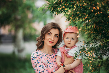 Young beautiful mother with small child in pink clothes on background of beautiful blooming tree in the open