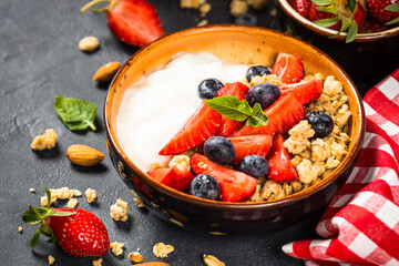 Greek yogurt granola with fresh berries on black stone table.