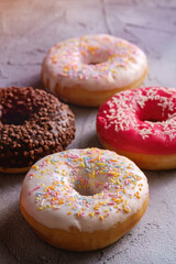 Chocolate, pink and vanilla donuts with sprinkles, sweet glazed dessert food on concrete textured background, angle view macro