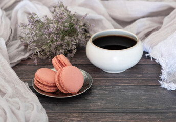 Cup of coffee with three strawberry macarons, on wooden table and violet flowers