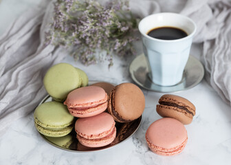 Cup of coffee with chocolate macaroons, strawberry and pistachios on marble table and violet flowers