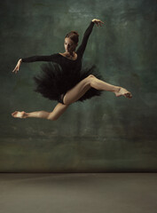 Balanced. Graceful classic ballerina dancing, posing isolated on dark studio background. Elegance black tutu. Grace, movement, action and motion concept. Looks weightless, flexible. Fashionable.