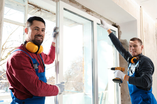 Workers using electric screwdriver for window installation indoors