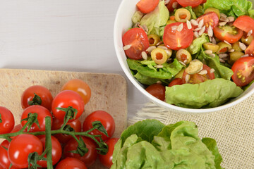 green lettuce with tomatoes, green olives and sunflower seeds in a white bowl