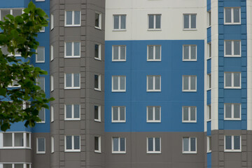Obraz premium A modern, newly-built multi-apartment multi-storey residential building in which no one lives and apartments are for sale. The facade of a blue building with still uninhabited windows against a backgr