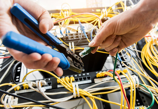 Network engineer working in server room. Connecting network cables to switches - Powered by Adobe