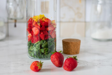 Strawberry lemonade with mint. Ingredients for lemonade in a bottle on white background. Strawberry, lemon zest, peppermint, water.