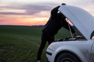 Obraz na płótnie Canvas Man standing near car with open hood on sunset. Car breakdown. Confused man stands with open hood with selective soft focus.