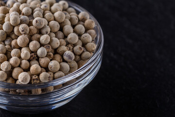 white peppercorns in glass bowl on stone background