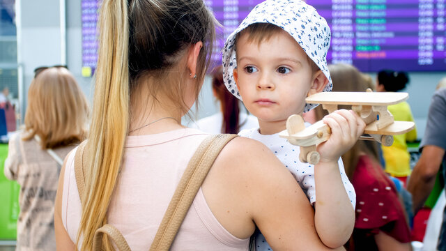 Portrait Of Sad Little Boy Hugging Mother In Airport And Holding Toy Airplane