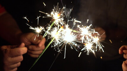 A group of friends lit sparklers together. People get ready for the holiday and light Bengal fires. The company of friends became in a circle. Hand with a sparkler closeup