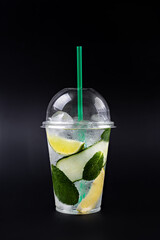 Lemonade to go cup with mint, lime, lemon and cucumber on black background, isolated