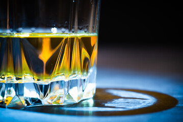 A glass of whiskey lit by a ray of light stands on a dark table and on a black background