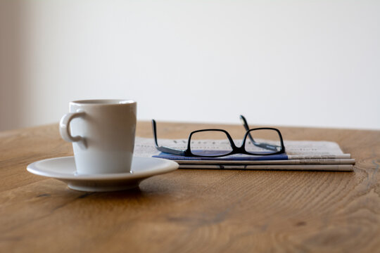 Eine Tasse mit Kaffee neben einen Zeitung und einer Brille auf einem Holztisch. Fertig zum lesen