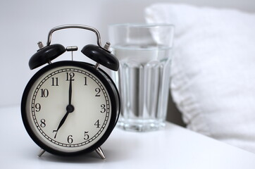 Clear glass of water for drinking on bed in the morning. An image of a retro clock showing 7:00 am....