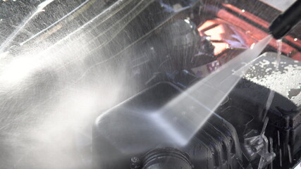 Washes away dirt from a car engine with a high-pressure water jet close-up. Special detergent for...