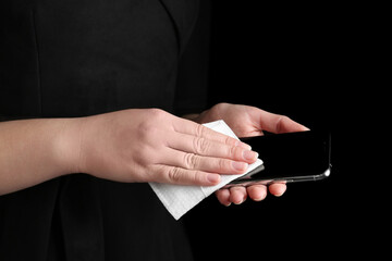 Woman cleaning mobile phone with antiseptic wipe on black background, closeup