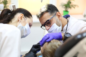 dentist is diagnosing the child while assistant in dental clinic