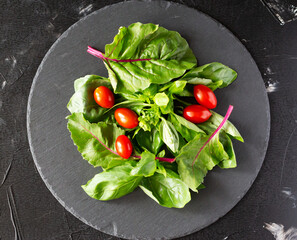 Fresh basil and mangold leaves and cherry tomatoes on round slate board . Healthy diet concept. Top view