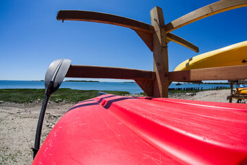 Kayaks in wooden stand outside near water with paddle