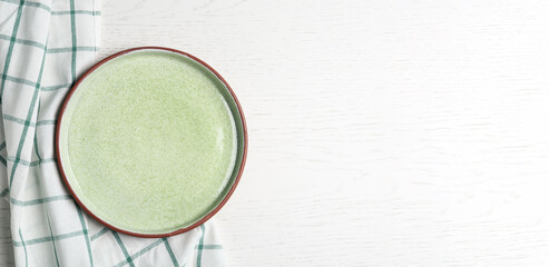 Empty light green plate and fabric on white wooden table, flat lay. Space for text
