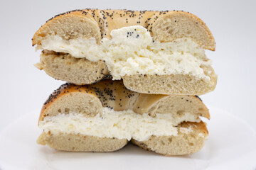 Cut In Half Poppy Seed Bagel with Cream Cheese on a White Plate with a White Background