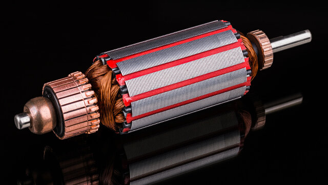 Inside of DC motor rotor with reflection on black background. Artistic still life of dismantled rotary electrical engine. Commutator, wire winding and transformer sheets on shaft. Full depth of field.