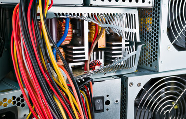 Inside of power supply unit with induction coils, heatsinks and transformer. Closeup of broken box of computer part in stack of used hardware. Hanging colored cables. Eco disposal of electronic waste.
