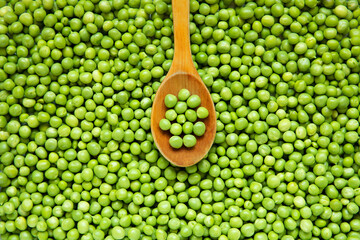 Wooden spoon on full of fresh green peas background.