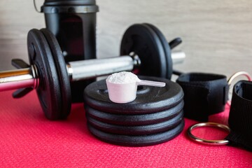 Plastic spoon or measuring scoop of whey protein on a dumbbell barbell stack next to the collected dumbbells. Concept of nutrition for bodybuilding and gaining muscle mass.