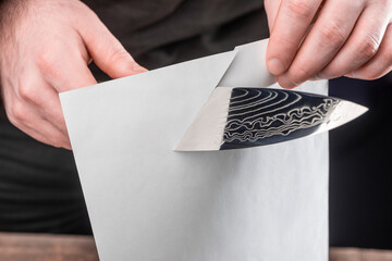 Man showing sharpness of a knife by cutting a thin paper sheet